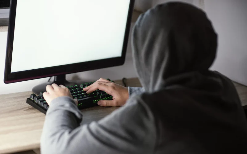 Jovem em frente a um computador de blusa cinza hackeando